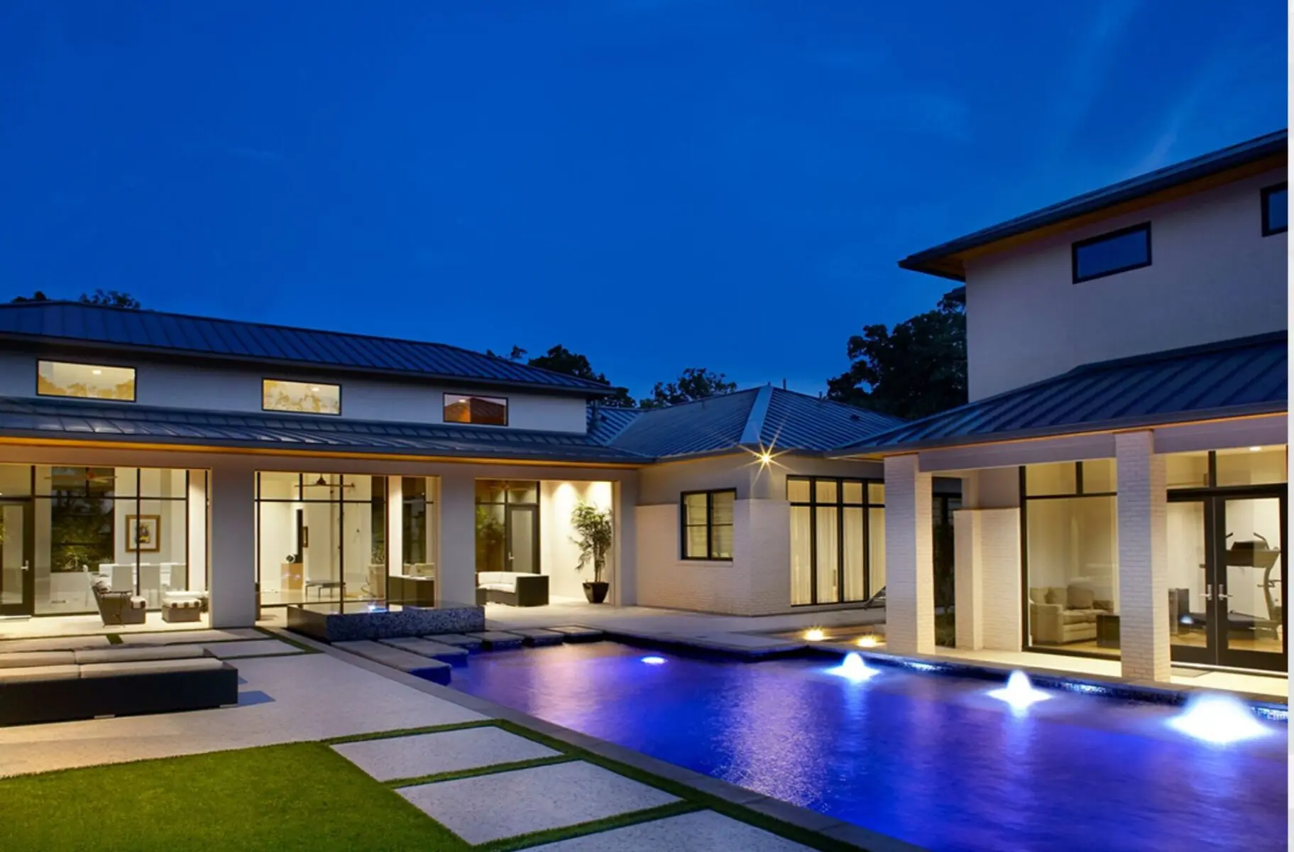 Modern custom pool with deck jets and night lighting beside a contemporary home