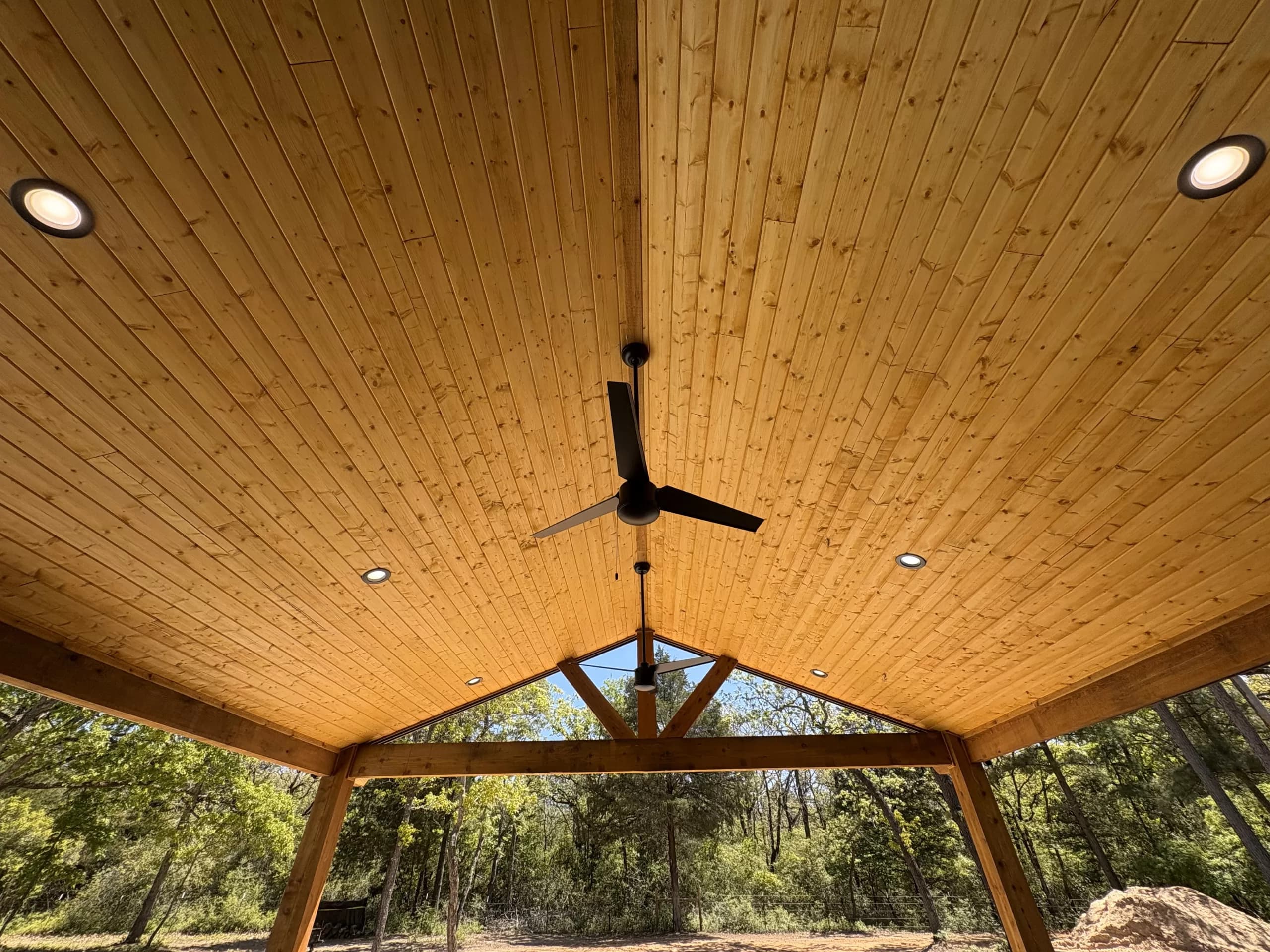 Wood ceiling and beams of a covered patio with recessed lights and a ceiling fan