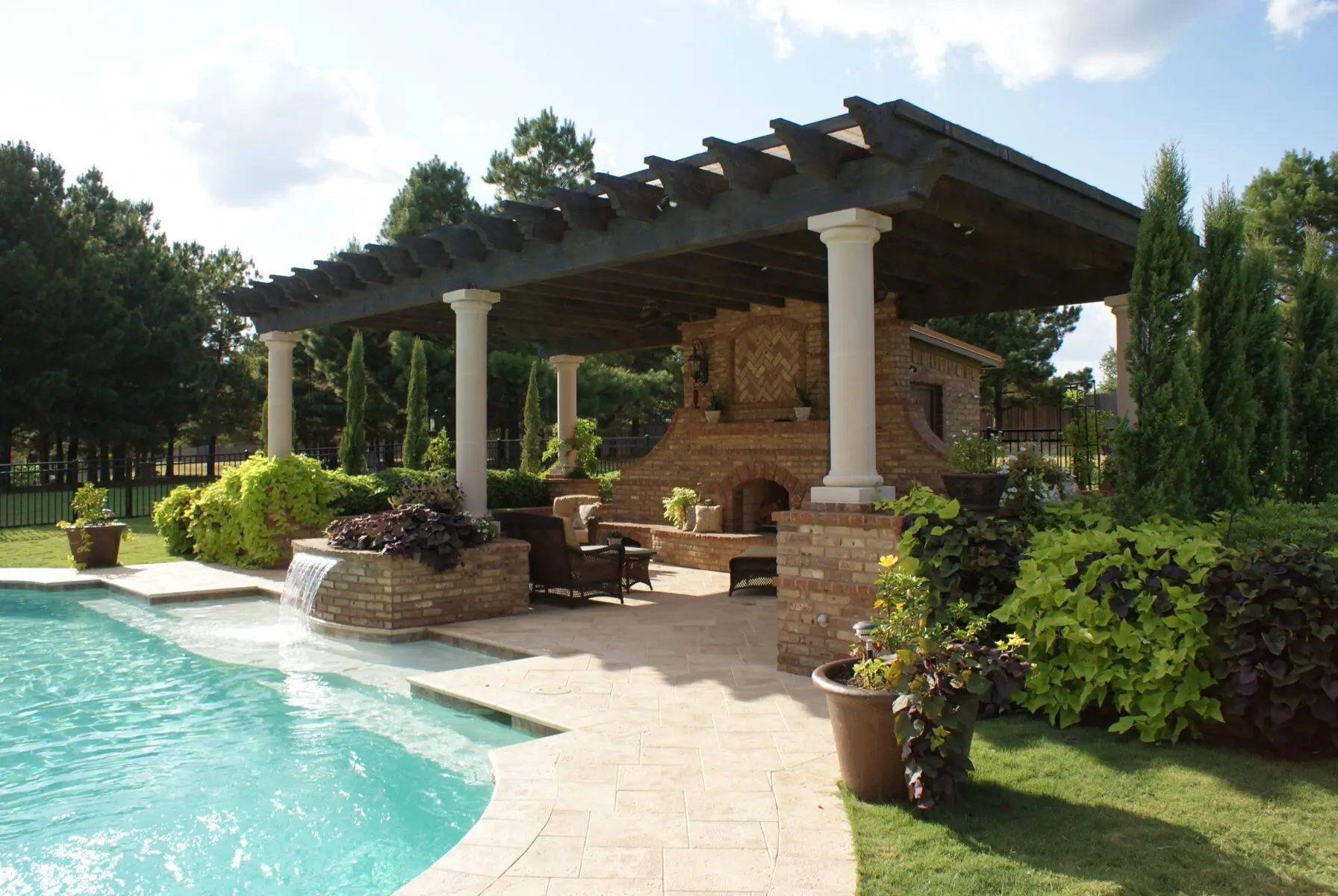 Pergola with stone columns and an outdoor fireplace beside a pool