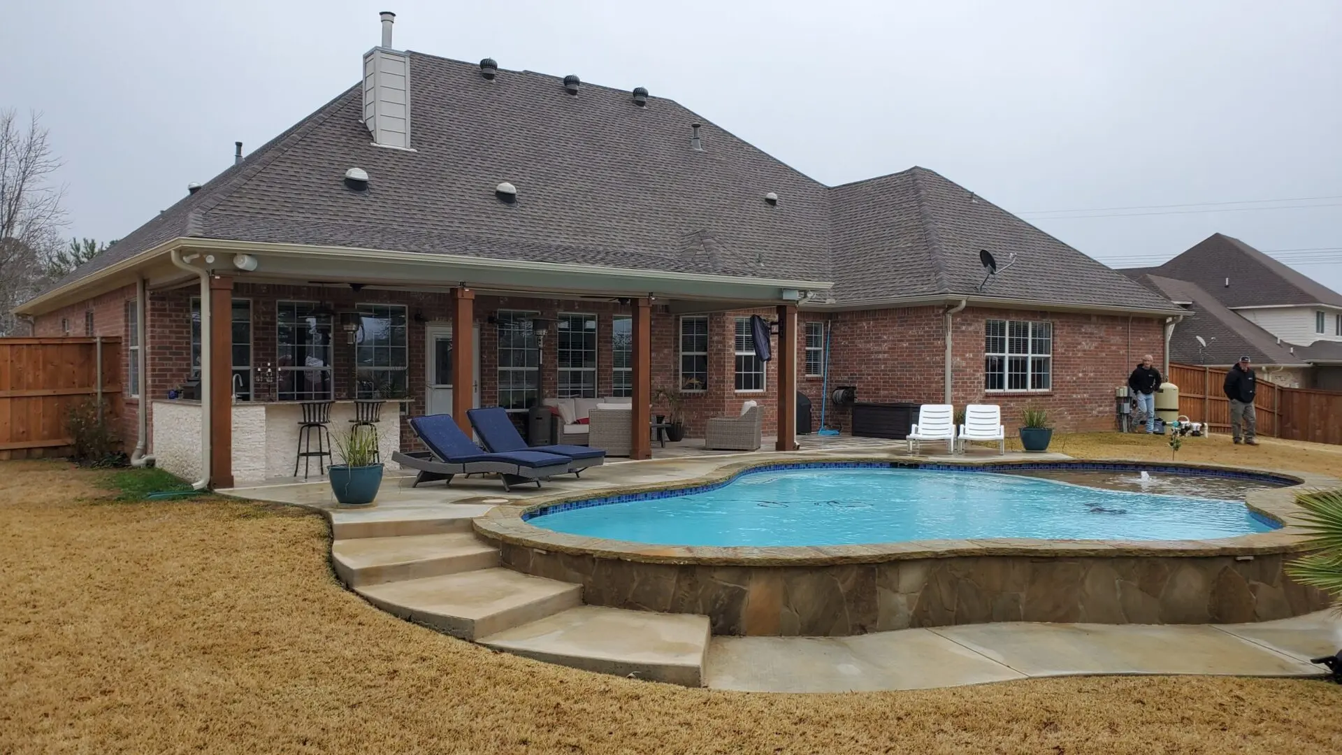 Raised freeform custom pool with flagstone steps beside a covered patio on a brick home